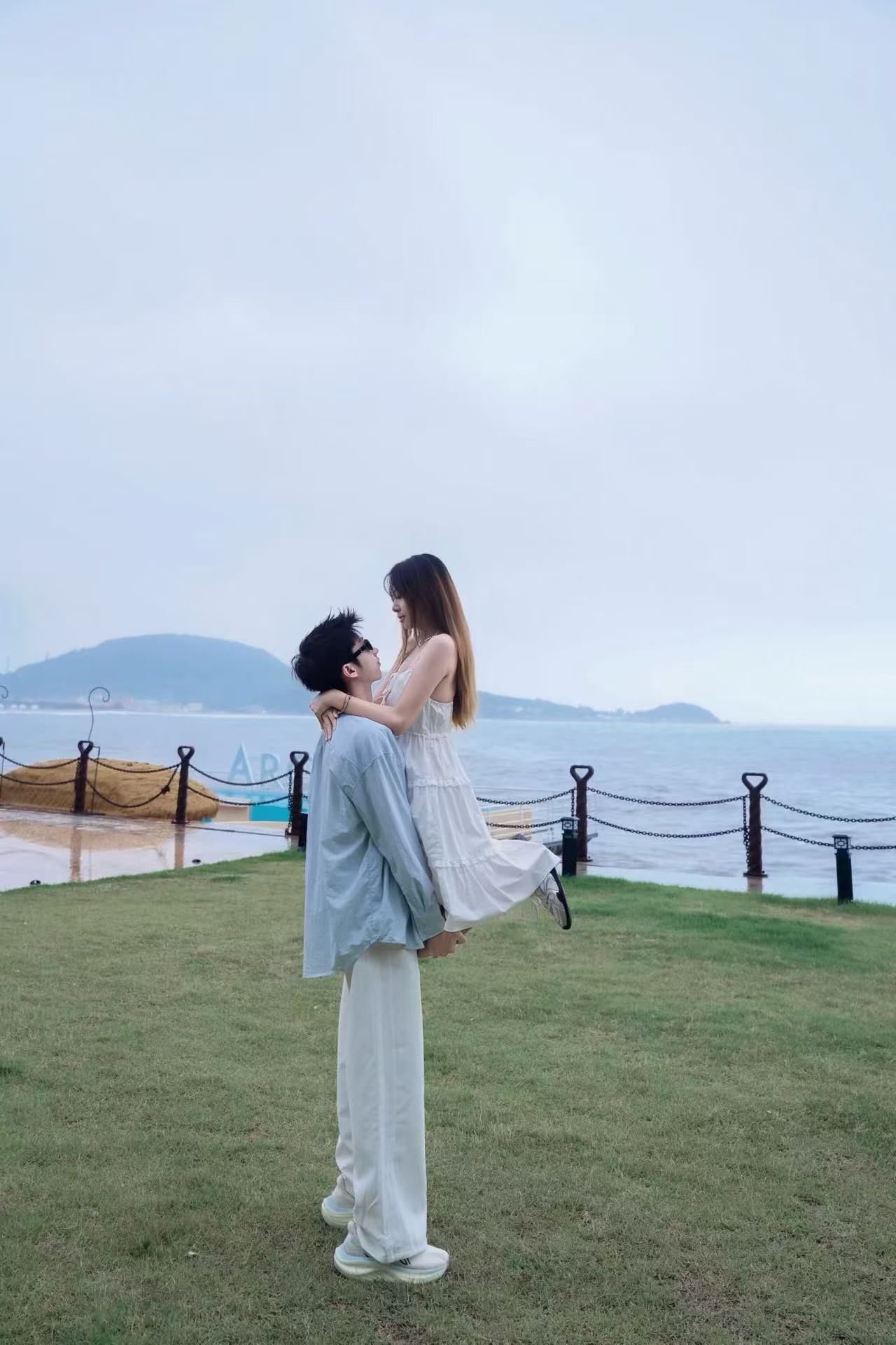 在青岛海边草地上的合照，男生抱着女生，背后是一望无际的海面